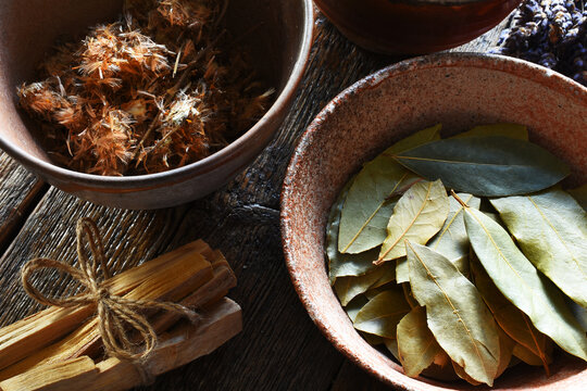 A top view image of dried arnica and bay leaves in hand made pottery bowls with palo santo. 