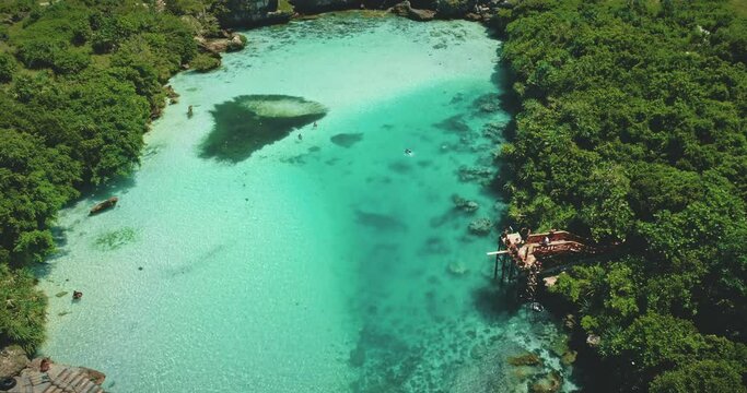 Tropical resort with emerald salt water lake of Weekuri, Indonesia, Asia. People recreation and swimming in saltwater lagoon at green tropic forest and grass. Cinematic rise up aerial view