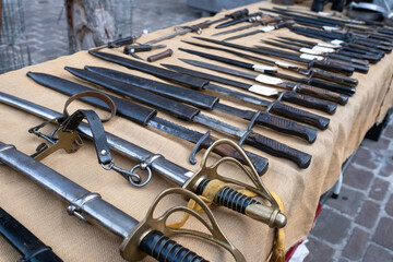All kinds of swords with scabbards in different sizes displayed on a table for sale on an antique...