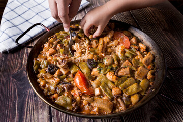A man's hand and a child's hand tasting paella.