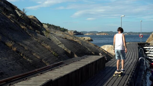 Young guy is longboarding skateboarding in the docks at the beach in Norway in Kjerringvik