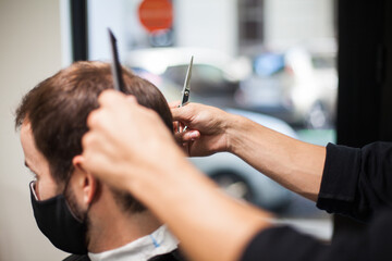 Man getting hair cut at the barber shop wearing protective mask during coronavirus pandemic