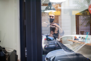 Man getting hair cut at the barber shop wearing protective mask during coronavirus pandemic