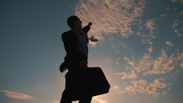 A businessman in a suit on top of a mountain. A successful person seeks victory, to achieve a goal, success. The concept of teamwork. Silhouette of man pulling emotionally hand up, symbol of victory.