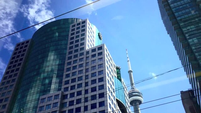 Passenger POV from moving city streetcar looking upwards at buildings with glimpse of CN tower In the distance