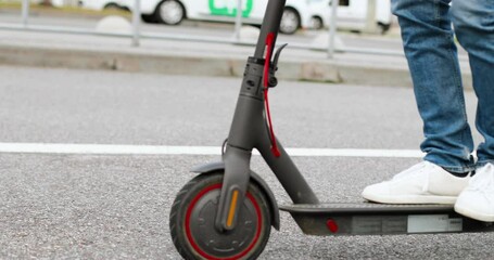 Close up of male feet in white sneakers standing on electric scooter an driding on road at city street. Man having fast ride in town. Modern vehicle. Urban transportation.