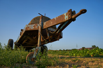 Fototapeta premium Old manure trailer, rusted drawbar in focus. Vegetable field.