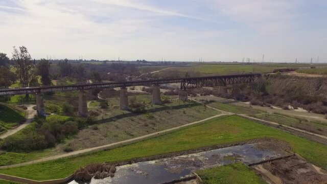 Aerial shot rises slowly as freight train crosses a train bridge over the San Joaquin River in Fresno, California.