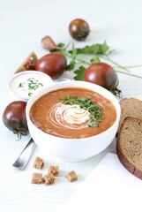 Black tomato puree soup with sour cream, croutons and parsley in a bowl on a white background