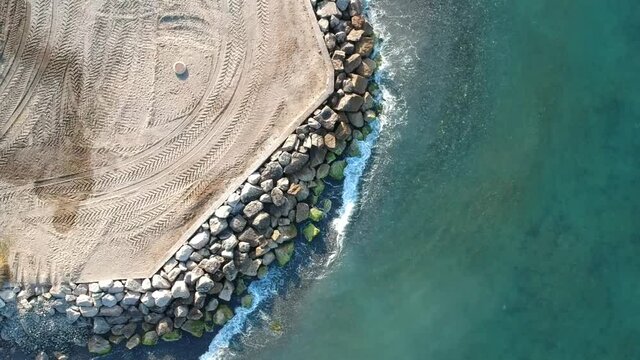 Aerial view of an ocean breakwater, rocky shoreline and tractor tracks