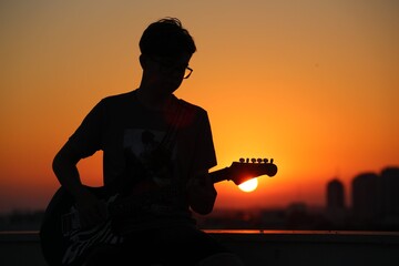 Young boy playing an acoustic guitar on the roof, sunset