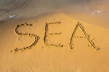The word SEA written on a yellow sandy beach near the sea