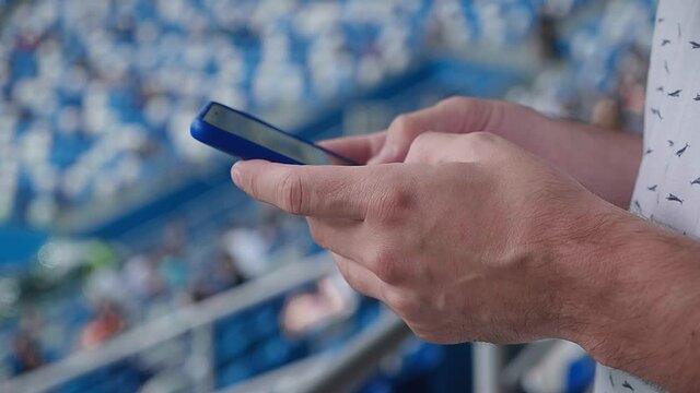 A young man writing a message on his phone during a match at the stadium. Mass event during coronavirus quarantine. Close-up of hands. High quality 4k footage