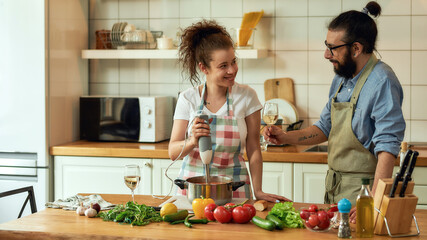 Young couple preparing a meal together in the kitchen. Italian man, chef cook looking at his girlfriend, holding a glass of white wine. Cooking at home, Italian cuisine