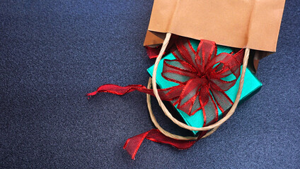 Top angle view green glitter gift box with red ribbon spill out of shopping bag on black table