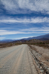 Desert route across the death valley. View of the dirt road, desert and mountains under a beautiful blue sky with clouds. 