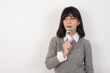 Very hungry Young businesswoman with retro short hair wearing casual clothes standing over isolated white background holding spoon into mouth dream of tasty meal