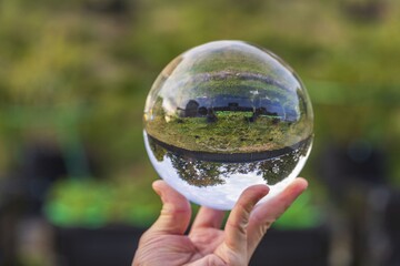 Close up macro view of hand holding crystal ball with inverted image of reen natural landscape.