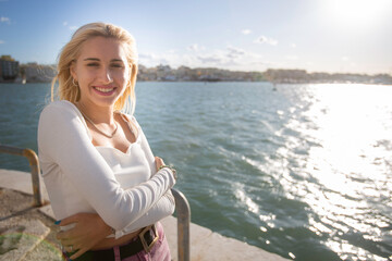 Outdoor, day. Portrait of an Italian woman with long blonde hair in a white low-cut top enriched by...