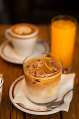 Two glasses and a cup with morning beverages (coffee - cappuccino, iced americano with milk, orange juice) on the wooden table in Florence, Tuscany, Italy. European breakfast