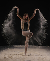 Beautiful sensual fit slim dancer in black body with long blond hair throwing dust, flour, powder...