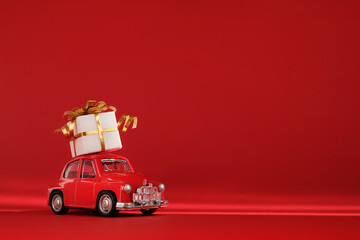 Red small retro toy car with gift on the roof on red background. Delivery. New Year, Christmas,...