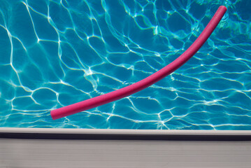 Pink pool noodle floating in a blue pool abstract