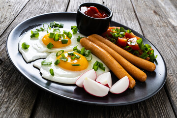 Breakfast - sunny side up egg, boiled sausages and vegetables served on wooden table
