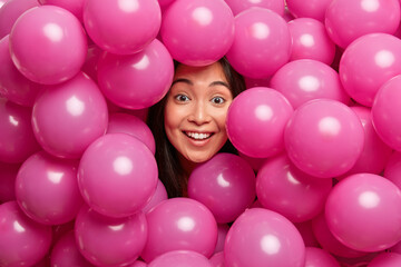 Fototapeta na wymiar Photo of beautiful brunette woman looks with positive unexpected experession at camera poses around many colorful balloons prepares for bachelorette party. Attractive Asian girl celebrates birthday