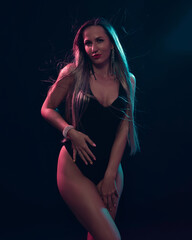 Beautiful attractive glamorous female in black body with blond long hair illuminated with colourful gel lights - turquoise and pink and wearing diamond earrings and bracelet
