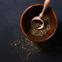 Miscela di erbe: peperoncino, aglio, erbe aromatiche in una ciotola su sfondo scuro.