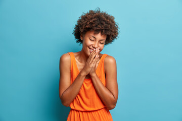 Overjoyed young Afro American woman laughs joyfully and keeps palms pressed together hears...