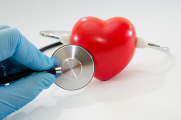 cropped view of doctor in latex gloves examining red heart with stethoscope on white background