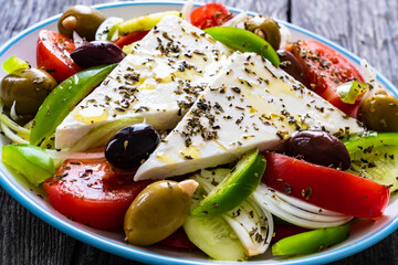 Fresh Greek salad - feta cheese, tomatoes, cucumber, red pepper, black olives and onion on wooden table
