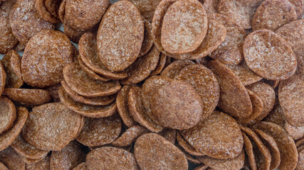 A pile of brown chocolate oval shaped flakes-muesli  lying on top of each other, a close-up shot. Food background for the design.