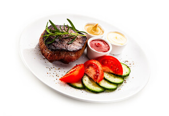 Barbecue beef steak with fresh tomatoes and cucumbers, mustard, mayonnaise and ketchup on white background
