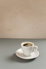 White cup with espresso coffee on a white saucer on a gray background. Selective focus. Copy space. Vertical orientation.