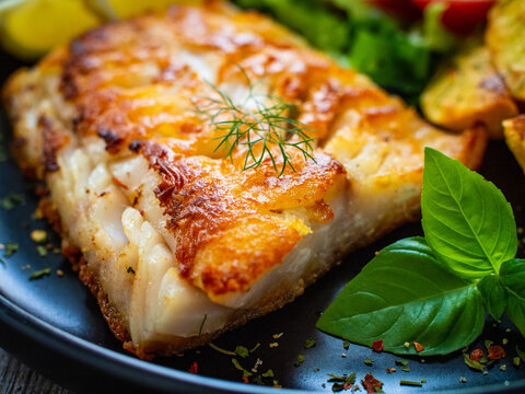 Fish dish - fried cod fillet with potatoes and vegetable salad on wooden table
