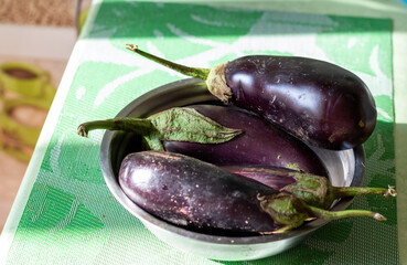 Blue fresh eggplants, aubergines in bowl on green table in sun light