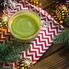 Green Japanese matcha tea in a transparent mug in Christmas decorations on a napkin with a zigzag...