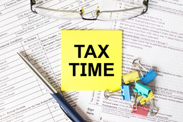 Yellow sticker with text Tax Time. Next to it is a blue pen with colored stationery clips and...