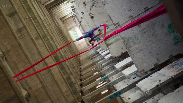 Athletic woman aerialist with steep stretch performs trick on canvases on background an atmospheric abandoned building. Does beautiful split. Extreme sport concept. Healthy lifestyle. Slow motion
