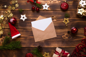Mail envelope made of craft paper with a white sheet for text on a wooden background with Christmas decor. A letter to Santa Claus, a wish list, a new year's dream, a gift. Flat lay, copy space