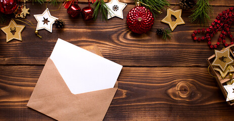 Mail envelope made of craft paper with a white sheet for text on a wooden background with Christmas decor. A letter to Santa Claus, a wish list, a new year's dream, a gift. Flat lay, copy space