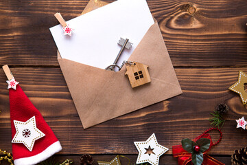 Christmas flat lay on a wooden background with keys to new house in the center with a envelope with a note sheet. New year, transfer, shares of the mortgage, the rental of a cottage. Space for text