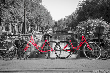 A picture of two red bikes on the bridge over the channel in Amsterdam. The background is black and white. 