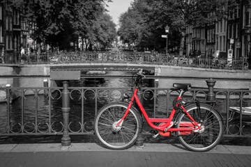 A picture of a red bike on the bridge over the channel in Amsterdam. The background is black and white. 