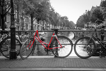 Obraz premium A picture of a red bike on the bridge over the channel in Amsterdam. The background is black and white. 