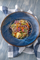 Vitamin salad from cabbage, carrots and olive oil. Natural delicious food. Greek cuisine menu. Still life in a marine style on a blue background.