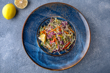 Vitamin salad from cabbage, carrots and olive oil. Natural delicious food. Greek cuisine menu. Still life in a marine style on a blue background.